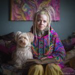 Alternative looking hippy style woman sitting down inside and boho home, wearing an Alex Tooth Radiant Bloom Sanctum Hoodie.
