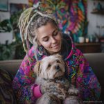 Alternative looking hippy style woman sitting down inside and boho home, wearing an Alex Tooth Radiant Bloom Sanctum Hoodie.