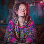 Alternative looking hippy style woman sitting down inside and boho home, wearing an Alex Tooth Radiant Bloom Sanctum Hoodie.