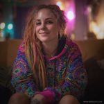 Alternative looking hippy style woman sitting down inside and boho home, wearing an Alex Tooth Radiant Bloom Sanctum Hoodie.