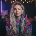Alternative looking hippy style woman sitting down inside and boho home, wearing an Alex Tooth Radiant Bloom Sanctum Hoodie.