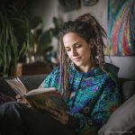 Alternative looking hippy style woman sitting down inside and boho home, wearing an Alex Tooth Emerald StarGate Sanctum Hoodie.