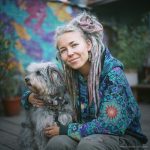 Colourful dreadlocked woman with a grey dog in front of a painted mural — visionary art by Alex Tooth.