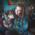 Alternative looking hippy style woman sitting down inside and boho home, wearing an Alex Tooth Emerald StarGate Sanctum Hoodie.