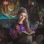 Alternative looking hippy style woman sitting down inside and boho home, wearing an Alex Tooth Inner Flight Sanctum Hoodie.