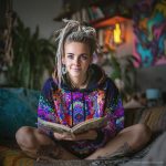 Alternative looking hippy style woman sitting down inside and boho home, wearing an Alex Tooth Inner Flight Sanctum Hoodie.