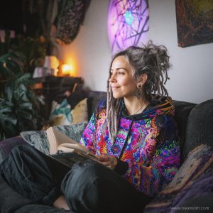 Vibrant woman with dreadlocks reading a book on a sofa in a colourful, artistic room— visionary art by Alex Tooth.