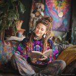 Alternative looking hippy style woman sitting down inside and boho home, wearing an Alex Tooth Inner Flight Sanctum Hoodie.