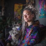 Alternative looking hippy style woman sitting down inside and boho home, wearing an Alex Tooth Inner Flight Sanctum Hoodie.