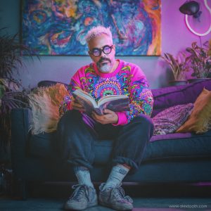 Reading colourful art book in a vibrant, psychedelic room— visionary art by Alex Tooth.