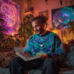 Cool looking alternative hippy style man sitting in a boho home reading a book wearing Alex Tooth Emerald StarGate Stillpoint Sweatshirt.