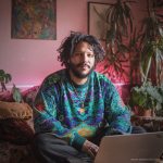 Cool looking alternative hippy style man sitting in a boho home reading a book wearing Alex Tooth Emerald StarGate Stillpoint Sweatshirt.
