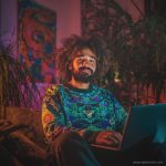 Cool looking alternative hippy style man sitting in a boho home reading a book wearing Alex Tooth Emerald StarGate Stillpoint Sweatshirt.