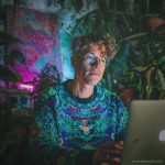 Cool looking alternative hippy style man sitting in a boho home reading a book wearing Alex Tooth Emerald StarGate Stillpoint Sweatshirt.