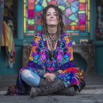 Alternative looking hippy style woman seated wearing an Alex Tooth Inner Flight Ritual Wrap shawl cover up.