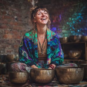 Alternative looking hippy style woman seated wearing an Alex Tooth Emerald StarGate Ritual Wrap shawl cover up.