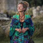 Alternative looking hippy style woman seated wearing an Alex Tooth Emerald StarGate Ritual Wrap shawl cover up.