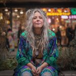 Alternative looking hippy style woman seated wearing an Alex Tooth Emerald StarGate Ritual Wrap shawl cover up.