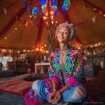 Alternative looking hippy style woman seated wearing an Alex Tooth Radiant Bloom Ritual Wrap shawl cover up.