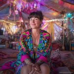 Alternative looking hippy style woman seated wearing an Alex Tooth Radiant Bloom Ritual Wrap shawl cover up.