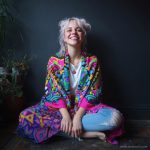 Alternative looking hippy style woman seated wearing an Alex Tooth Radiant Bloom Ritual Wrap shawl cover up.
