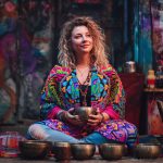 Alternative looking hippy style woman seated wearing an Alex Tooth Radiant Bloom Ritual Wrap shawl cover up.
