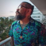 Cool looking hippy type alternative style man standing outside wearing and Alex Tooth Emerald StarGate Island Flow Hawaiian Shirt.