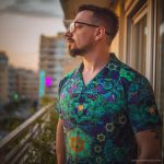 Cool looking hippy type alternative style man standing outside wearing and Alex Tooth Emerald StarGate Island Flow Hawaiian Shirt.