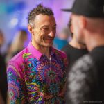 Smart looking alternative hippy style man standing in a inside social function setting wearing an Alex Tooth Radiant Bloom InnerLight Shirt.