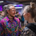 Smart looking alternative hippy style man standing in a inside social function setting wearing an Alex Tooth Radiant Bloom InnerLight Shirt.