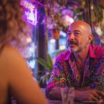 Smart looking alternative hippy style man sitting inside a boho cafe / restaurant setting wearing an Alex Tooth Radiant Bloom InnerLight Shirt.