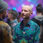 Smart looking alternative hippy style man standing in a inside social function setting wearing an Alex Tooth Emerald StarGate InnerLight Shirt.