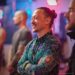 Smart looking alternative hippy style man standing in a inside social function setting wearing an Alex Tooth Emerald StarGate InnerLight Shirt.