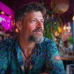 Smart looking alternative hippy style man sitting inside a boho cafe / restaurant setting wearing an Alex Tooth Emerald StarGate InnerLight Shirt.