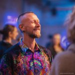 Smart looking alternative hippy style man standing in a inside social function setting wearing an Alex Tooth Inner Flight InnerLight Shirt.