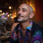 Smart looking alternative hippy style man sitting inside a boho cafe / restaurant setting wearing an Alex Tooth Inner Flight InnerLight Shirt.
