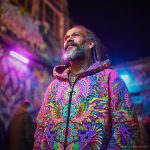 Alternative hippy looking man standing outside wearing Alex Tooth Radiant Bloom Pathfinder Jacket.