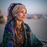 Edgy looking alternative hippy woman smiling, sitting down outside, wearing Alex Tooth Emerald StarGate Waylight Scarf.