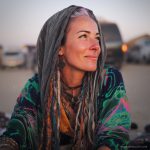 Edgy looking alternative hippy woman smiling, sitting down outside, wearing Alex Tooth Emerald StarGate Waylight Scarf.