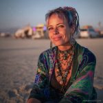 Edgy looking alternative hippy woman smiling, sitting down outside, wearing Alex Tooth Emerald StarGate Waylight Scarf.