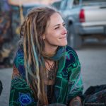 Edgy looking alternative hippy woman smiling, sitting down outside, wearing Alex Tooth Emerald StarGate Waylight Scarf.