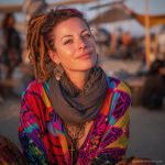 Edgy looking alternative hippy woman smiling, sitting down outside, wearing Alex Tooth Inner flight Waylight Scarf.