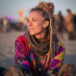 Edgy looking alternative hippy woman smiling, sitting down outside, wearing Alex Tooth Inner flight Waylight Scarf.