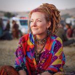 Edgy looking alternative hippy woman smiling, sitting down outside, wearing Alex Tooth Inner flight Waylight Scarf.