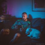 Man chilling on sofa with dog reading, wearing wearing Alex Tooth Emerald StarGate Long Sleeved Balance Tee T-Shirt.