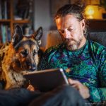 Man chilling on sofa with dog reading, wearing wearing Alex Tooth Emerald StarGate Long Sleeved Balance Tee T-Shirt.