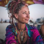 Edgy looking alternative hippy woman smiling, sitting down outside, wearing Alex Tooth Radiant Bloom Waylight Scarf.