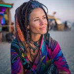 Edgy looking alternative hippy woman smiling, sitting down outside, wearing Alex Tooth Radiant Bloom Waylight Scarf.