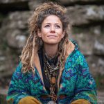 Alternative hippy boho style woman sitting down inside wearing buckle up fleece lined Alex Tooth Emerald StarGate Vision Robe.