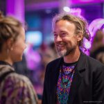 Man at social function, wearing wearing Alex Tooth Radiant Bloom Long Sleeved Balance Tee T-Shirt underneath his blazer.